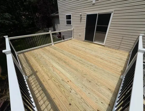 Wood deck with white railing posts and black balusters leading to a sliding door