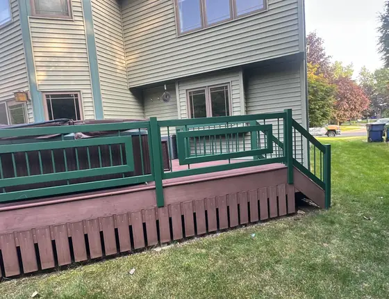 Raised deck with green painted railing and built in benches behind a home
