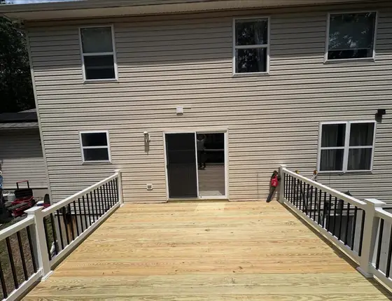 New pressure treated wood deck with black balusters and white posts behind a two story home