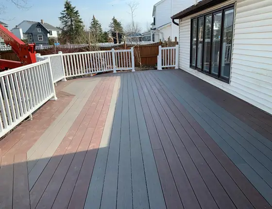 Two tone composite deck with white vinyl railing beside a sunroom