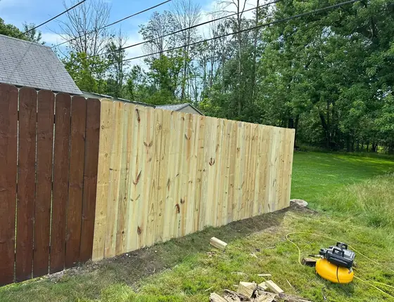 New fence installation with an air nailer resting on the lawn