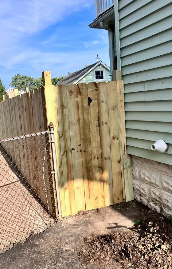 New wood gate between a house and a chain link fence