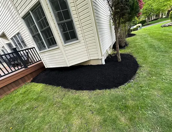 Black mulch bed curving along a deck and siding