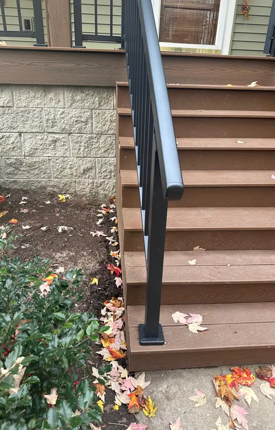 Brown composite stairs with a black handrail beside a home