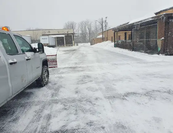 White pickup with a plow clearing a commercial parking lot