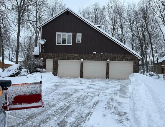 Truck with a plow blade clearing a driveway in front of a three car garage