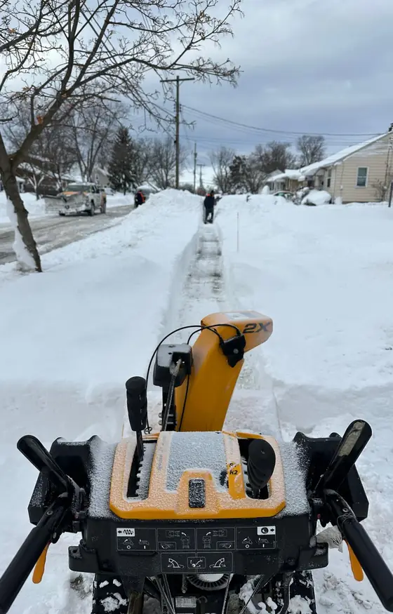Snow blower clearing a long sidewalk through deep snow
