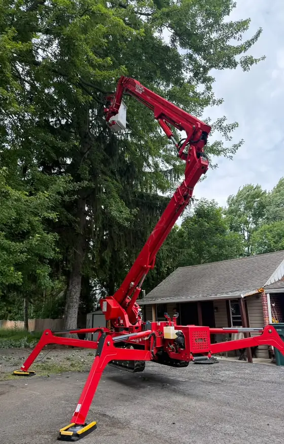 Red spider lift on a driveway for tree removal near a garage